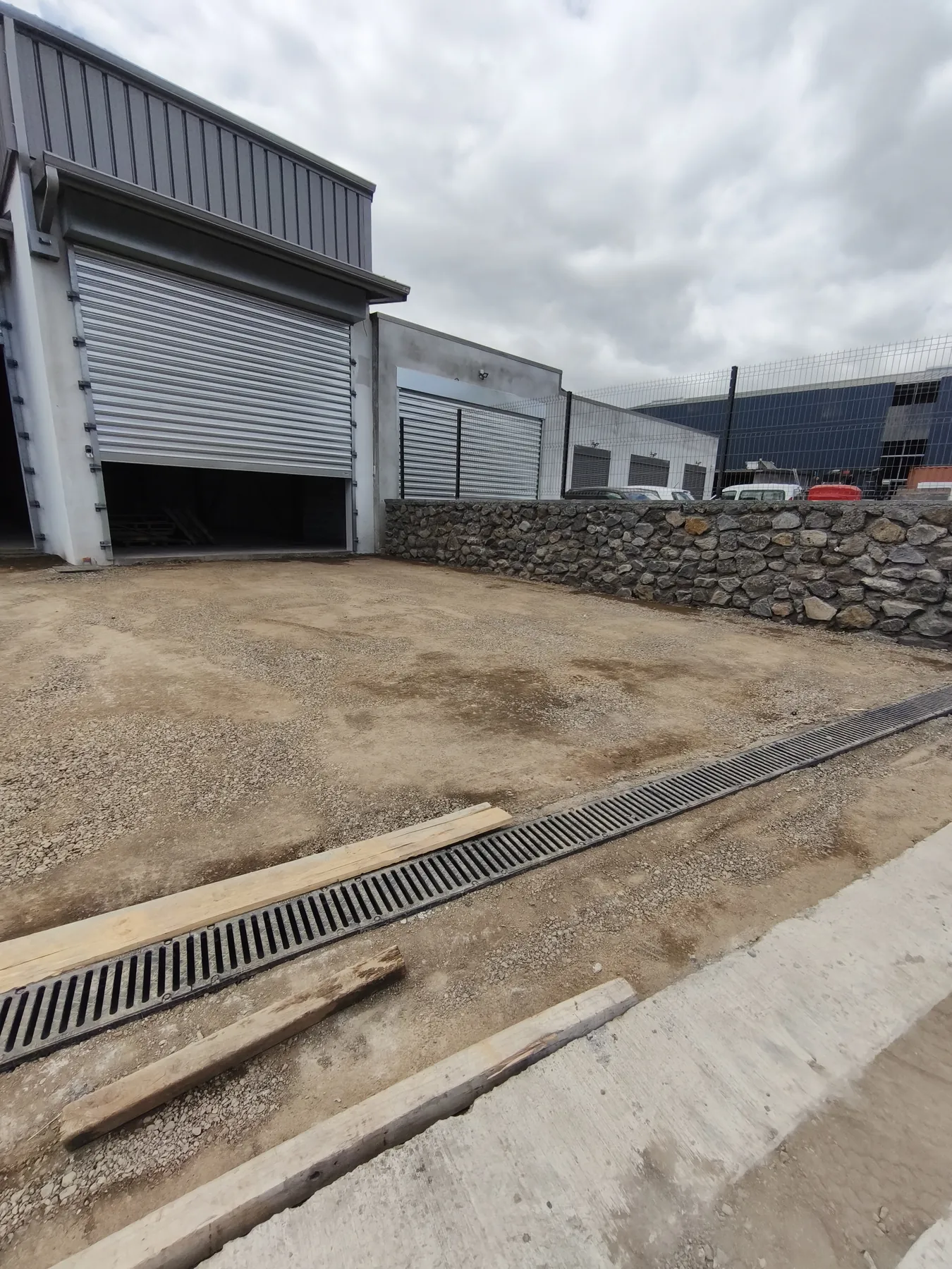 Abords du bâtiment industriel : enrobé, caniveau, clôture en moellons